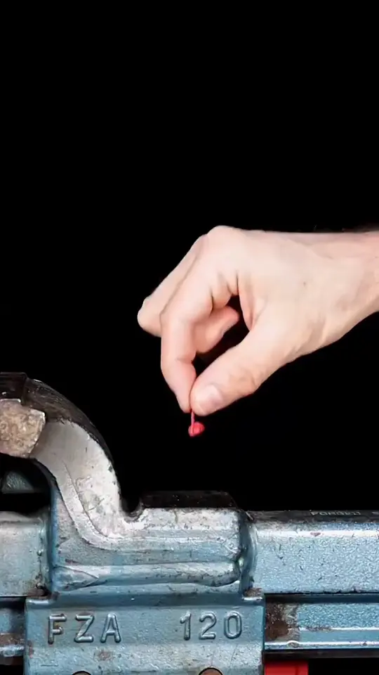 A hand sets something tiny under an industrial press and lets go