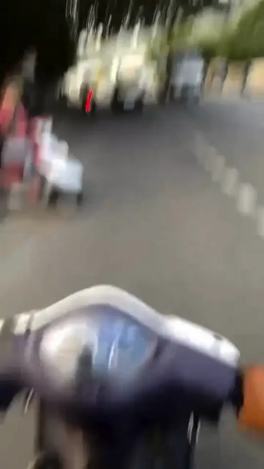A helmet camera whips along a tree-lined road as traffic streams past